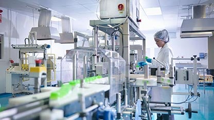 Worker inspecting products on production line in pharmaceutical factory -card